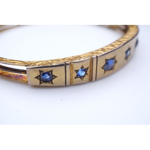 284 - A Victorian sapphire bangle, late 19th century, of hinged design, the front set with a sequence of o... 