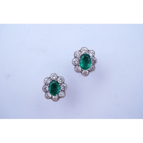 294 - A pair of emerald and diamond earrings, each of cluster design, set with an oval emerald within a mi... 