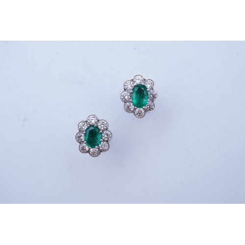 294 - A pair of emerald and diamond earrings, each of cluster design, set with an oval emerald within a mi... 