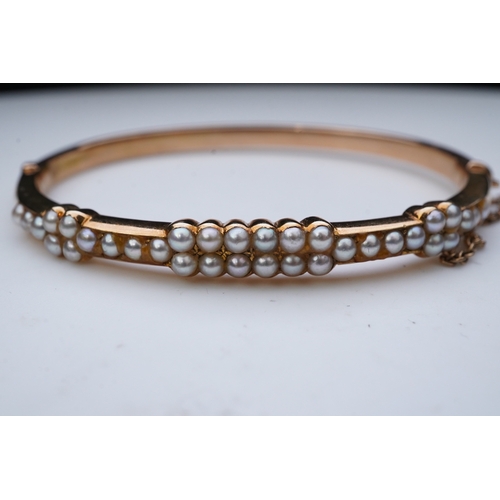 318 - An Edwardian seed pearl bangle, early 20th century, of hinged design, set to the front with half see... 