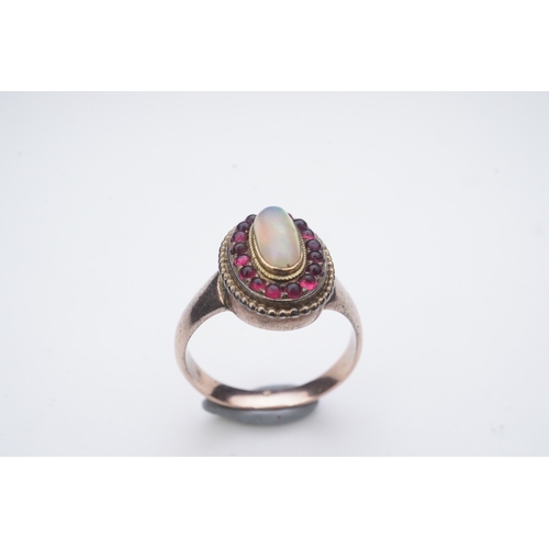 338 - An opal and garnet ring, of cluster design, set with an oval cabochon opal within a border of caboch... 