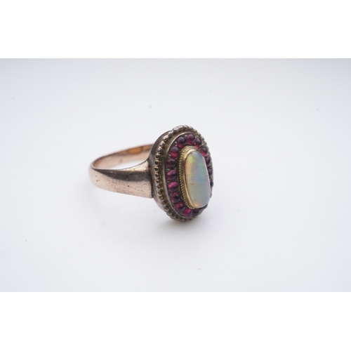 338 - An opal and garnet ring, of cluster design, set with an oval cabochon opal within a border of caboch... 