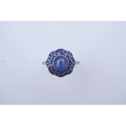 453 - A sapphire ring, of Art Deco inspiration, set with a cabochon sapphire within a floral double border... 