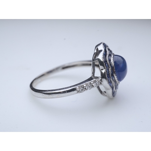 453 - A sapphire ring, of Art Deco inspiration, set with a cabochon sapphire within a floral double border... 