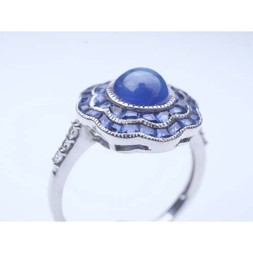 453 - A sapphire ring, of Art Deco inspiration, set with a cabochon sapphire within a floral double border... 