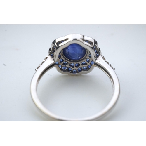 453 - A sapphire ring, of Art Deco inspiration, set with a cabochon sapphire within a floral double border... 