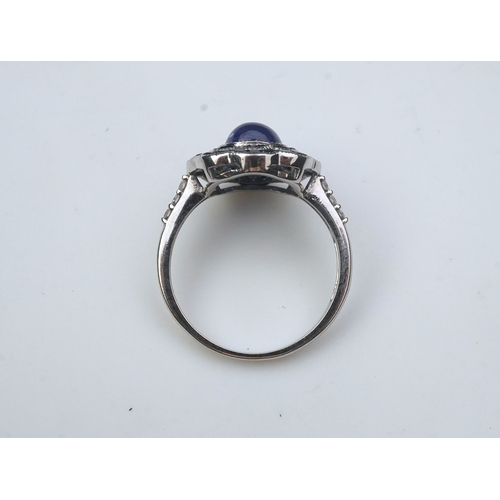 453 - A sapphire ring, of Art Deco inspiration, set with a cabochon sapphire within a floral double border... 