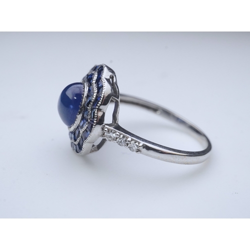 453 - A sapphire ring, of Art Deco inspiration, set with a cabochon sapphire within a floral double border... 