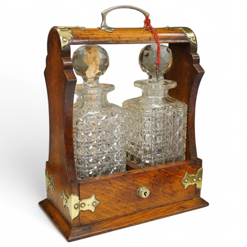 1374 - A brass mounted two bottled oak tantalus, 24cm wide, 33cm high. Condition - fair to good