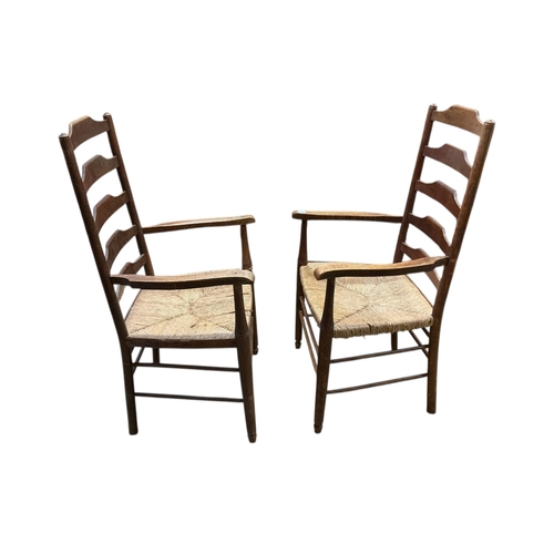 1085 - A pair of Arts & Crafts oak ladderback rush seat elbow chairs, width 62cm, depth 47cm, height 108cm... 
