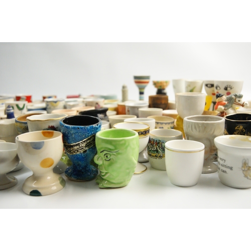 65 - A Large Collection of Ceramic and Glass Egg Cups Including Novelty and Souvenir ExamplesAn extensi... 