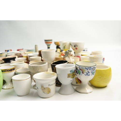 65 - A Large Collection of Ceramic and Glass Egg Cups Including Novelty and Souvenir ExamplesAn extensi... 
