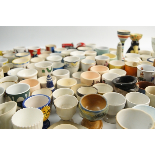 65 - A Large Collection of Ceramic and Glass Egg Cups Including Novelty and Souvenir ExamplesAn extensi... 