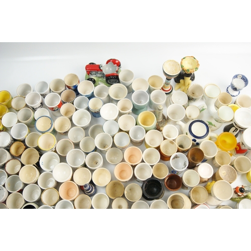 65 - A Large Collection of Ceramic and Glass Egg Cups Including Novelty and Souvenir ExamplesAn extensi... 