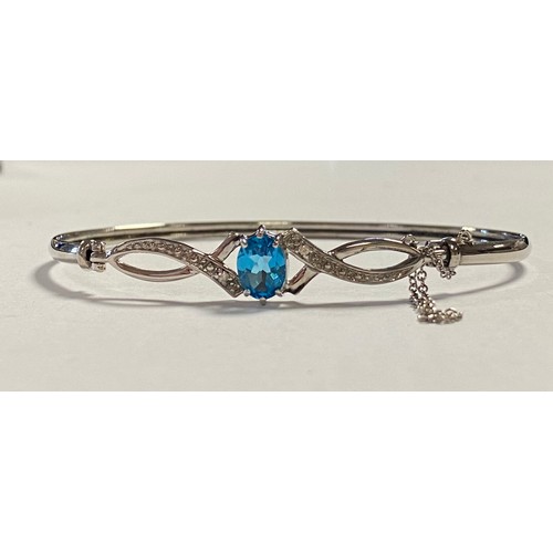 33 - A white gold and gem set bangle, set with an oval blue topaz and diamond points in 9ct white gold -