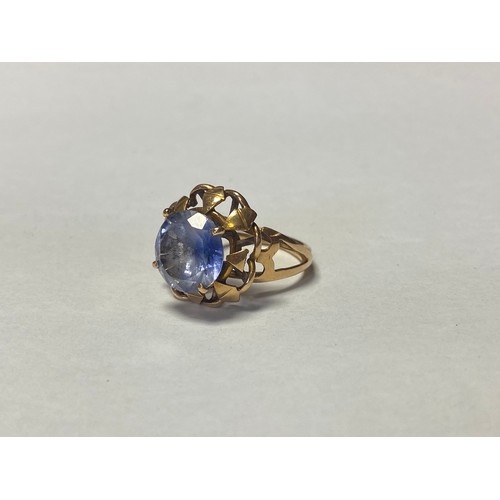 18 - A yellow metal ring, set with a large circular blue sapphire in circular frame and pierced shoulders... 