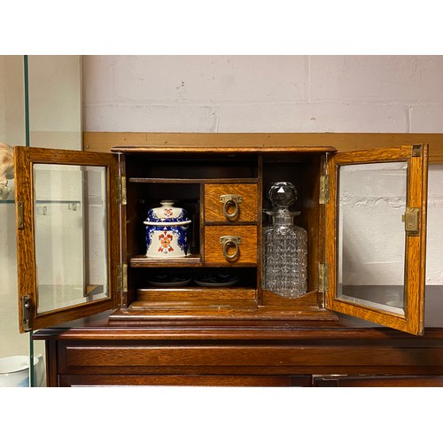 131 - An Edwardian oak smoking/drinking compendium cabinet, with two glazed doors enclosing pair of decant... 