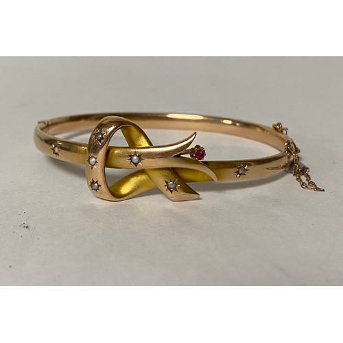 94 - A gem set gold bangle, set with a ruby and seed pearls in knotwork motif -