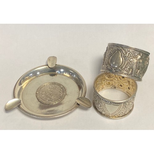 45 - A white metal ashtray, inset with a South American coin, and two napkin rings -