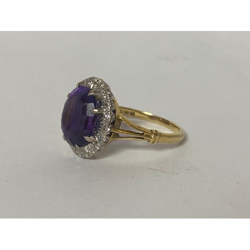 1 - An 18ct gold dress ring, set with an oval purple stone in a border of small diamonds -