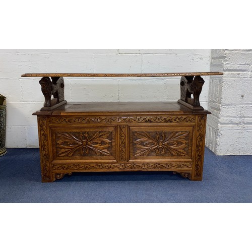 322 - An oak monks bench, with carved decoration, lion supports and lift top seat -