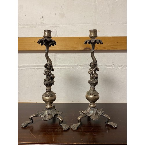 25 - A pair of white metal candlesticks, each with figural support on three legs -