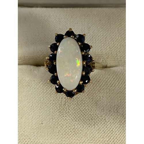 17 - An opal and sapphire dress ring, set with an oval opal in a border of sapphires, to 9ct gold mount -