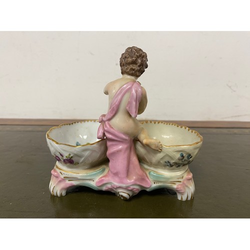 113 - A 19th century Dresden style sweetmeat dish, modelled as a putto between oval baskets -