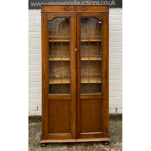 300 - A 1920's oak bookcase, with two leaded glass doors enclosing shelves, on bun feet -