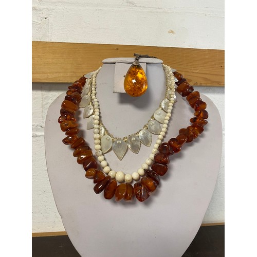 37 - An amber necklace, a white coral bead necklace, a mother-of-pearl necklace and an amber coloured pen... 