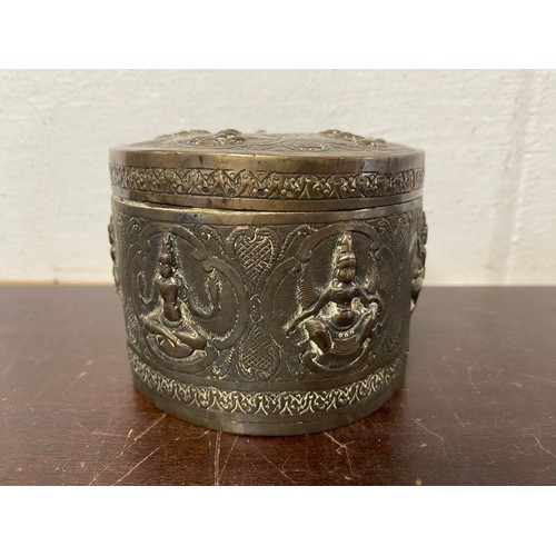 53 - An Indian white metal cylindrical box and cover, repousse decorated with figures -