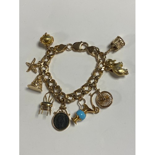 73 - A 14ct gold charm bracelet, suspending an array of charms, some stamped 14k, some hallmarked for 9ct... 