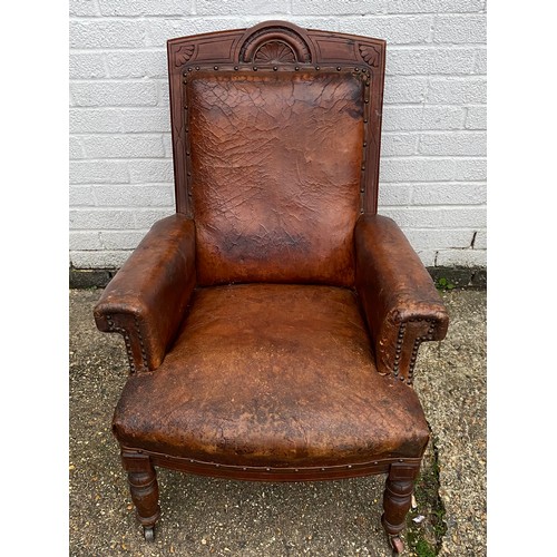A late Victorian leather library chair, with carved frame and low turned legs and casters -