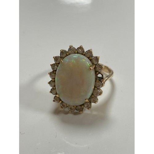 144 - An opal set dress ring, the large oval cabochon in a border of clear stones (1 missing) in 18 carat ... 