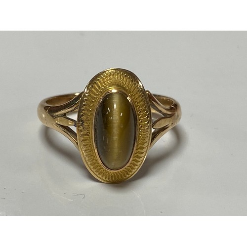 169 - A yellow metal dress ring, set with an oval tigers eye cabouchon -
