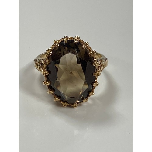 A modern dress ring, set with an oval smokey quartz in textured yellow metal mount -