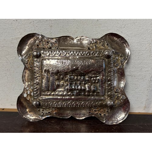 53 - A white metal dish, with repousse landscape detail and pierced surround, together with a silver spoo... 