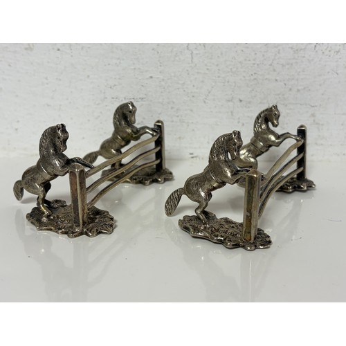 7 - A pair of silver plated knife rests each cast as horses at a three bar fence -