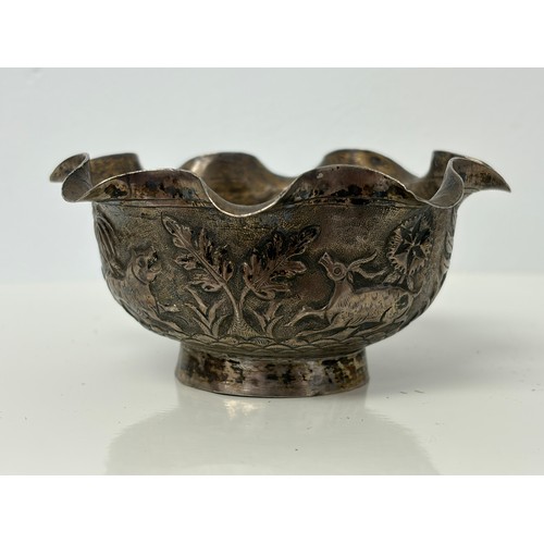 10 - An Indian white metal bowl, with wavy rim, decorated in the round with animals in a landscape -