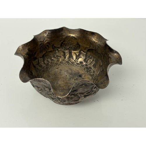10 - An Indian white metal bowl, with wavy rim, decorated in the round with animals in a landscape -