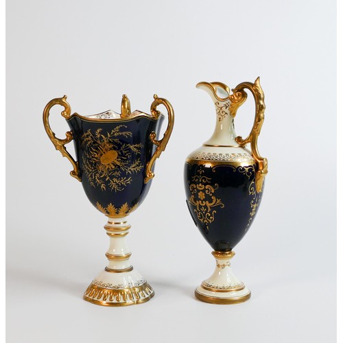 1625 - Coalport tri handled urn and handled ewer, both gilded & hand painted with panels of landscape scene... 