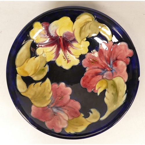 148 - Moorcroft Hibiscus on Blue Ground Shallow Footed Bowl, chip to rim, diameter 24.5cm