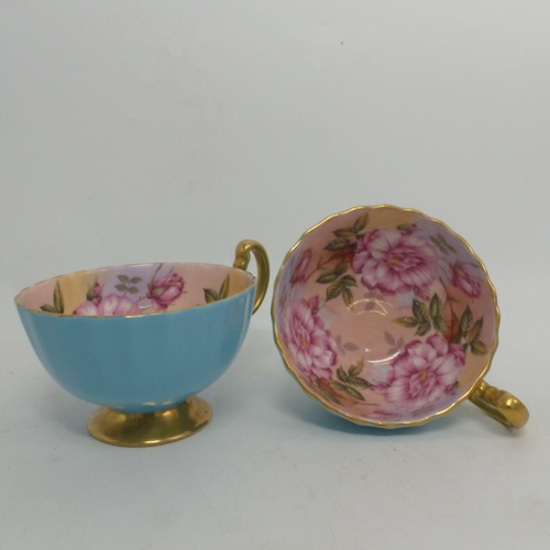 17 - Aynsley, Two Blue Ground Gilt Teacups with full internal image of roses. (2)