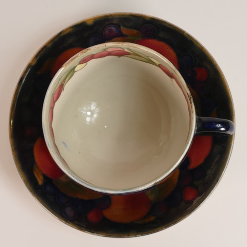 1260 - William Moorcroft tea cup and saucer in the Pomegranate design, cup decorated inside on cream ground... 