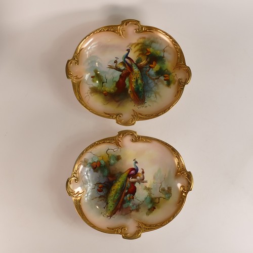 1289 - A pair of Royal Worcester comports, each shaped, gilded and hand painted with roosting Peacocks, one... 