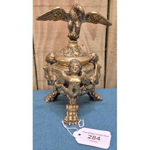284 - Antique heavy brass ink well pot; Lid designed with an eagle finial. Body detailed with three cherub... 