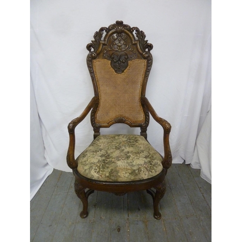 16 - A heavily carved walnut cane backed armchair with upholstered seat on four scroll legs