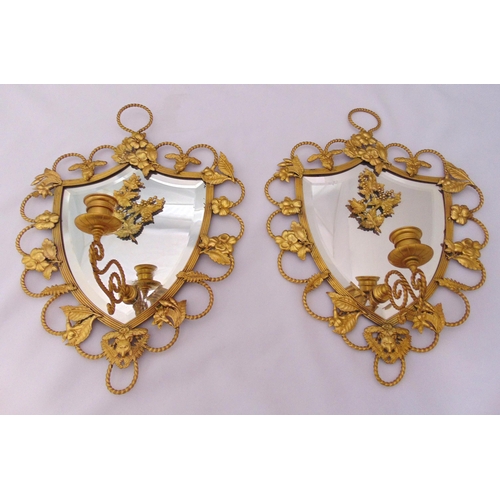 22 - A pair of gilt metal shield shaped mirror backed wall sconces decorated with leaves, flowers and scr... 