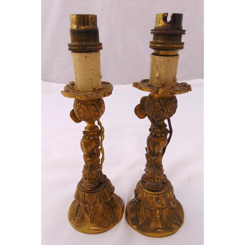 26 - A pair of late 19th century brass candlesticks in the form of stylised dolphins on raised circular b... 