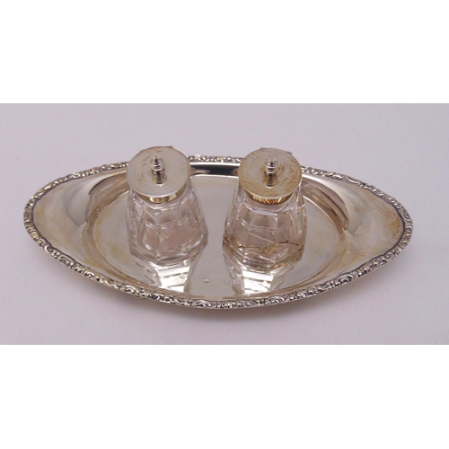 424 - A hallmarked silver ink stand oval with scroll chased border on three pierced bracket feet with two ... 